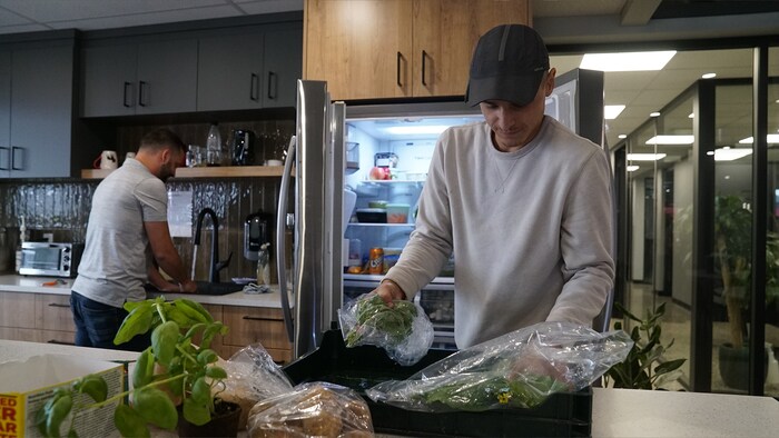 Un jeune homme vide un bac de légumes sur un comptoir dans la cuisine d'une entreprise.