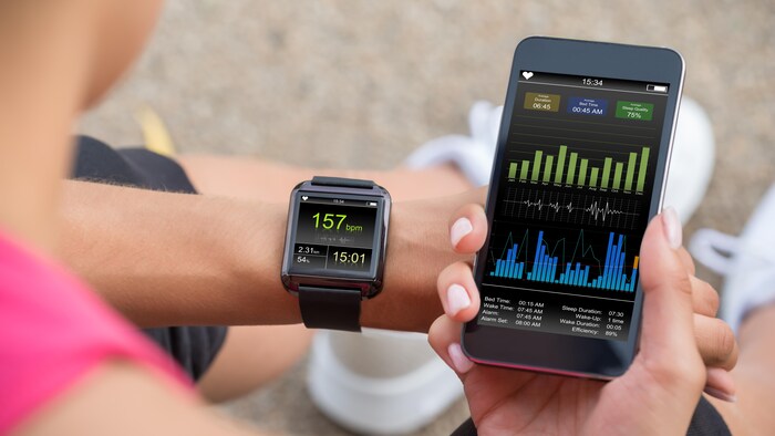 Une femme consulte son téléphone et sa montre connectée en s'entraînant.