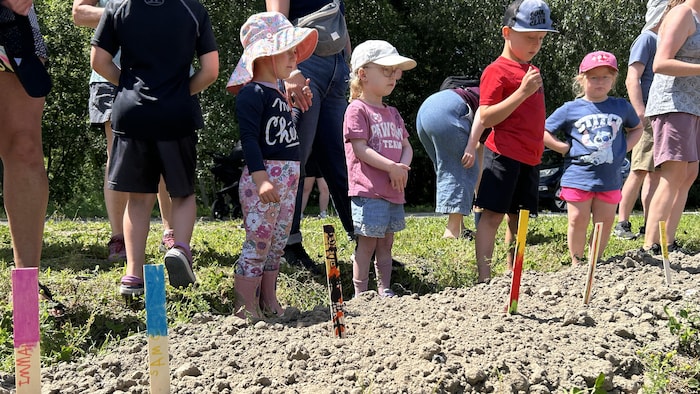 Des enfants se tiennent devant une rangée de bâtonnets colorés plantés dans la terre.