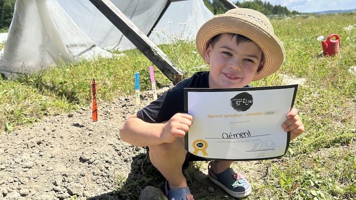 Un petit garçon tient un « diplôme » d'apprenti agriculteur.