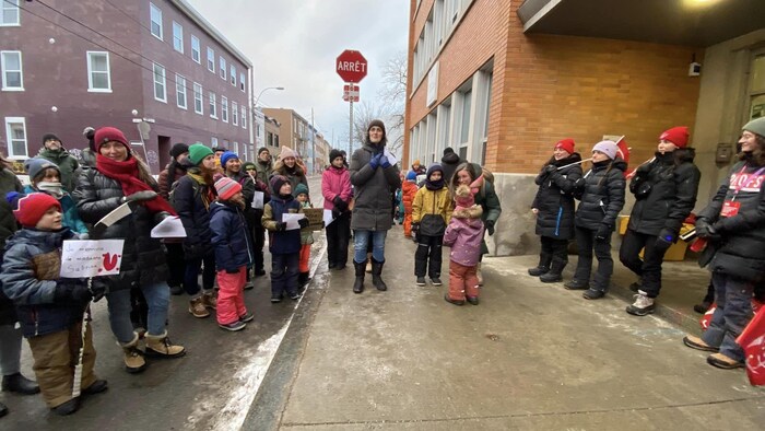 Des parents et leurs enfants sont dehors devant des professeurs en grève.
