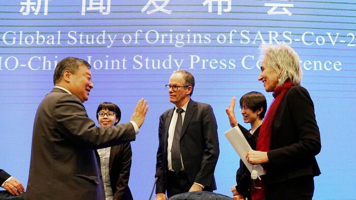 Five panelists standing around, waving goodbye on stage after giving a WHO press conference on the origin of COVID-19.