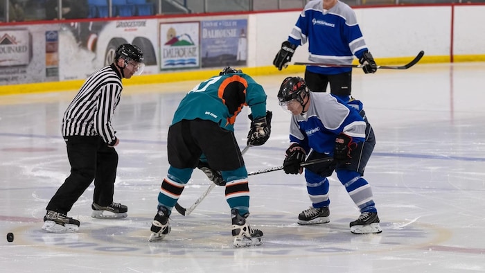 Un arbitre et trois joueurs de hockey sur la glace.