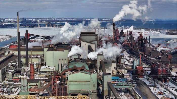 Image aérienne de l'aciérie d'ArcelorMittal à Hamilton, une usine avec de nombreuses cheminées qui crachent de la fumée 