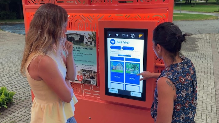 Deux personnes regardent la tablette interactive installée sur l'arche.