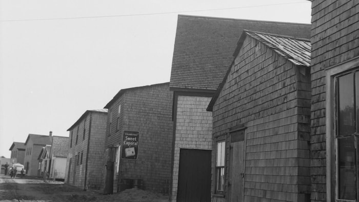 Une photo en noir et blanc montre plusieurs bâtiments en bardeaux de bois alignés.