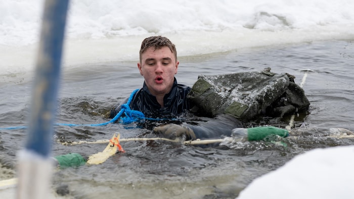Un soldat nage dans une eau encerclée de glace et de neige. 