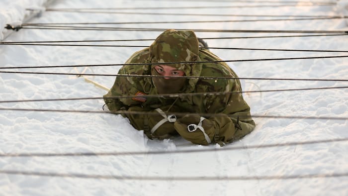 Un militaire en tenue de combat rampe sur un sol enneigé.