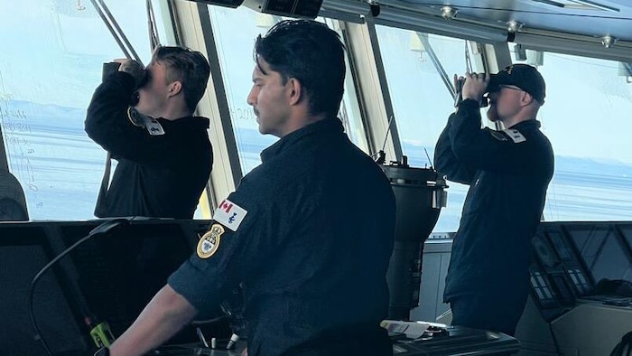 Sur un bateau deux personnes scrutent l'horizon avec des jumelles.