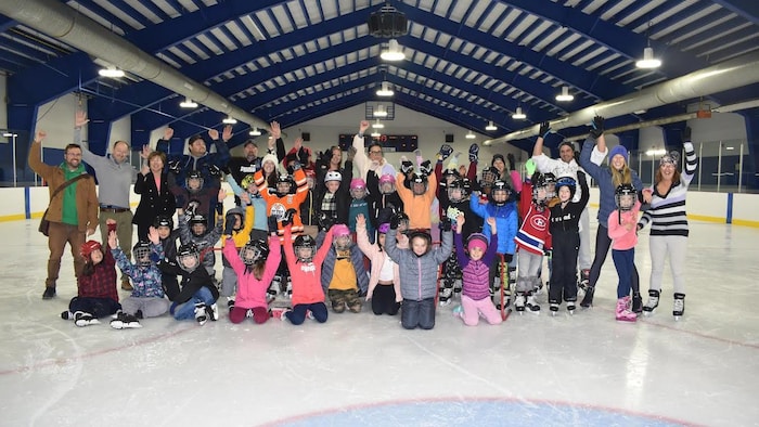 Plusieurs enfants et quelques adultes, bras en l'air, affichent leur joie en prenant une photo de groupe sur la patinoire de l'Aréna Kiwanis.