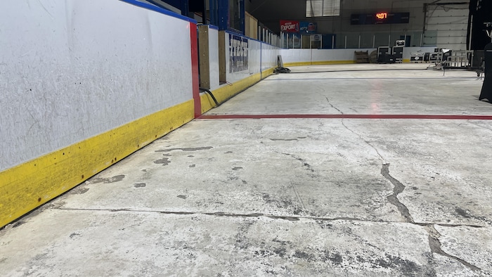 La surface de jeu en béton, qui accueille la glace en hiver, est craquelée et les bandes sont usées.
