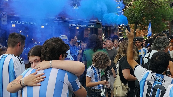 Des partisans se prennent dans les bras devant une fumigène bleue.