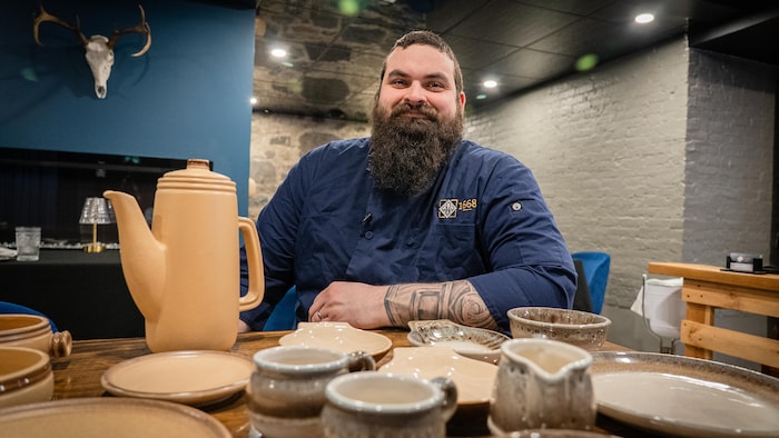 Un homme assis avec devant lui de la vaisselle sur une table.