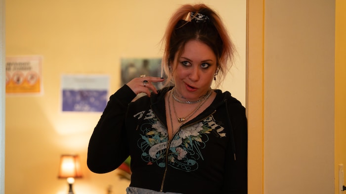 Une femme fait une grimace, appuyée sur le cadre d'une porte.