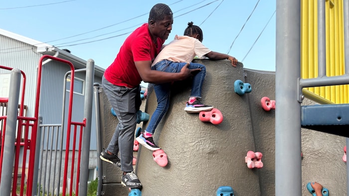 Un homme aide un enfant a grimper sur un module de jeux.