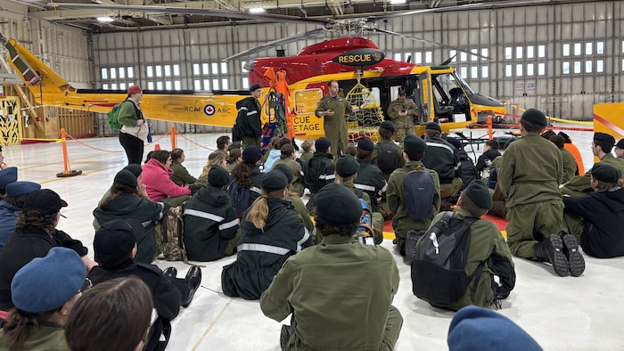 Des cadets sont assis devant un hélicoptère.