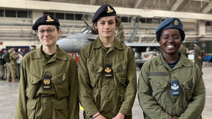 Trois cadets posent dans un hangar.