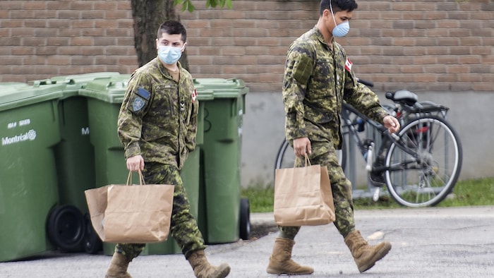 Des membres des Forces armées canadiennes transportent des sacs bruns.