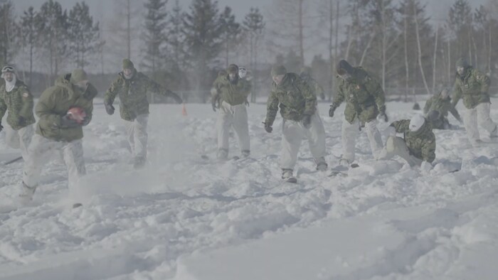 Une dizaine de soldats canadiens jouant au football avec des skis au pied.