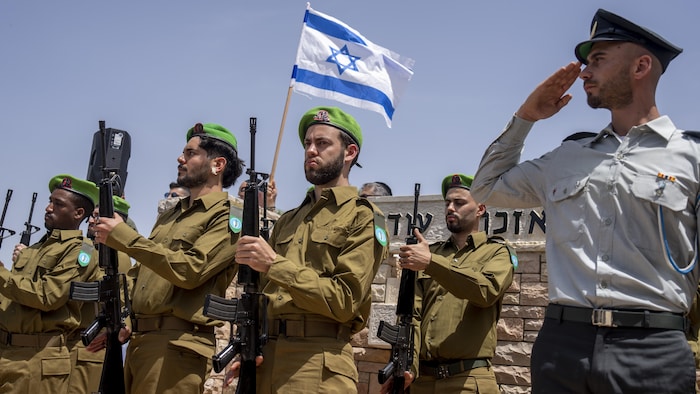 Des soldats debout, l'un d'eux portant un drapeau d'Israël.