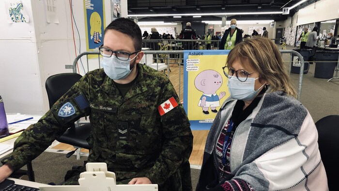 Un militaire travaille à l'ordinateur sous la supervision d'une femme.