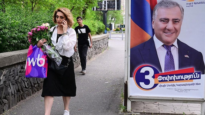 Une femme au téléphone marche devant une affiche d'un candidat.