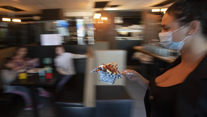 Une jeune serveuse portant un couvre-visage transporte un petit panier de pommes de terre frites qu'elle tient avec un bâtonnet.