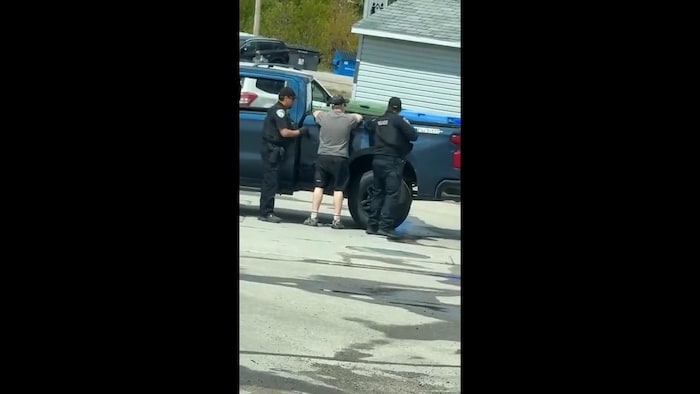 Un homme appuyé sur son véhicule se fait arrêter par des policiers.