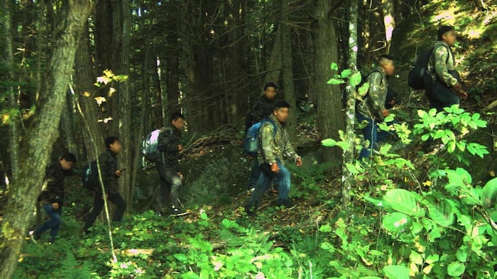 Un petit groupe d'hommes portant des sacs à dos marche dans une forêt.