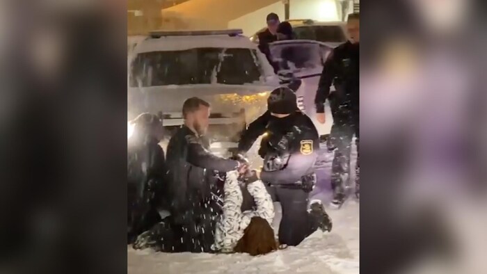 Des policiers maîtrisent une jeune femme au sol, dans la neige.