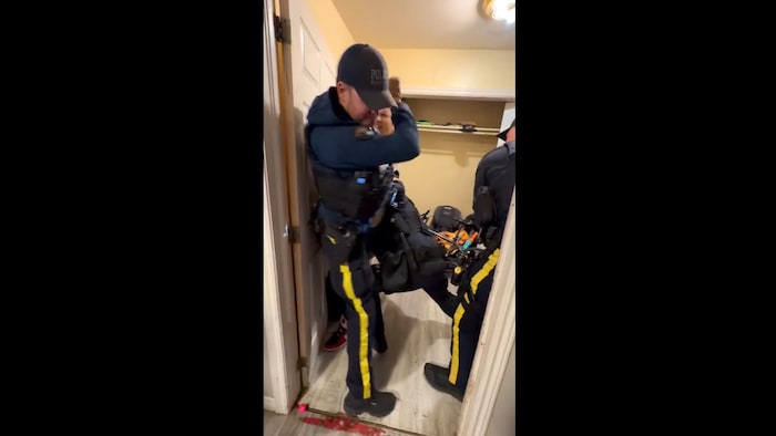 Un gendarme en uniforme détourne la tête et se protège le visage avec son bras. On entrevoit un homme en civil derrière lui.