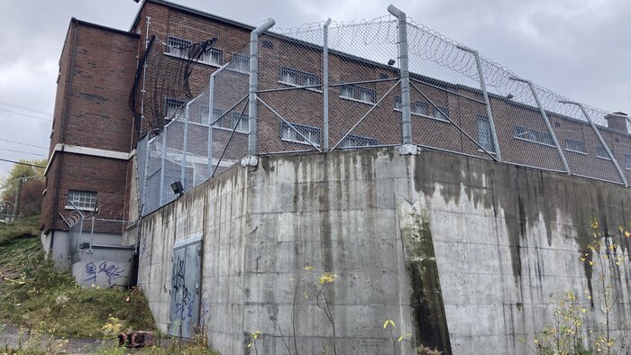 Un mur de béton et une haute grille ceinturent la cour arrière de la prison.
