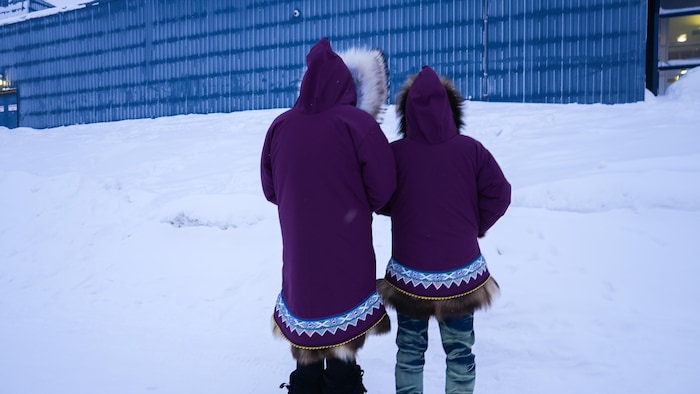 Deux hommes portant des parkas de femmes et vus de dos.