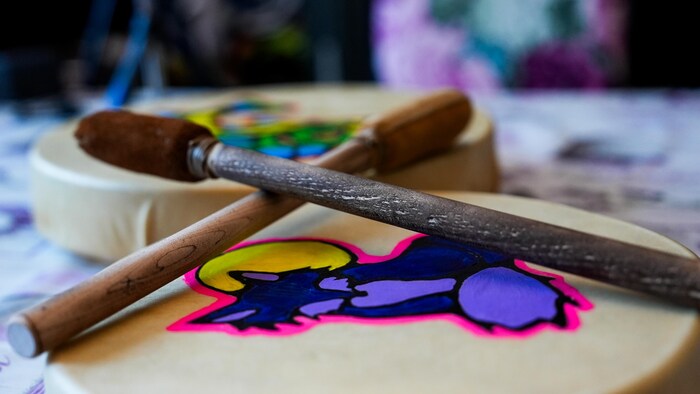 Deux tambours ornés de peintures d'animaux et avec deux baguettes en bois au-desssus.