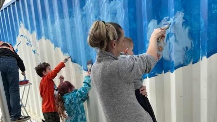 Une femme et des enfants sont en train de peindre un conteneur. 