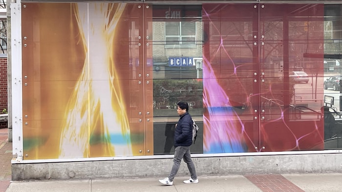 Un homme marche devant des oeuvres qui tapissent les murs de verre d'une station de métro.