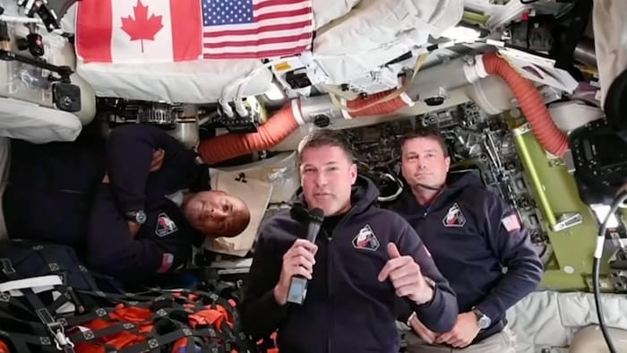 Jeremy Hansen parle dans un micro, entouré de deux autres astronautes, dans la capsule Orion.