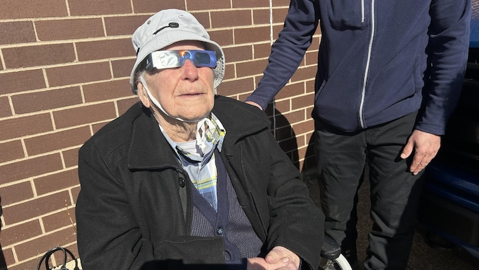Un centenaire avec des lunettes d'observation pour éclipse regarde vers le ciel. 