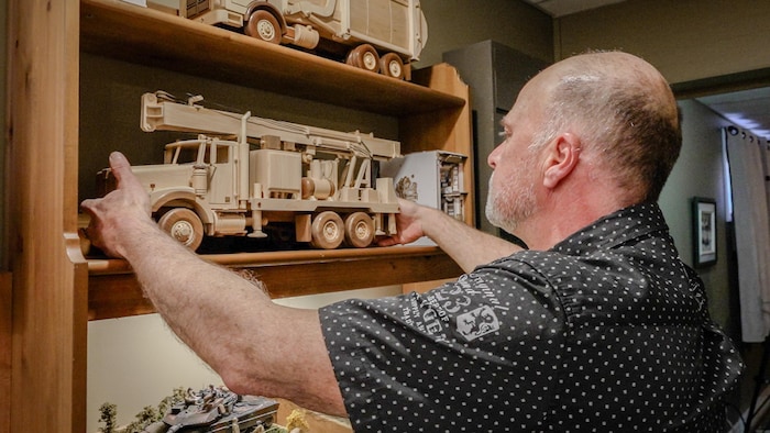 Un homme prend dans ses mains une reproduction d'un camion, muni d'une foreuse pour puits artésiens. 