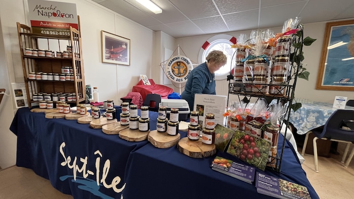 Une artisane travaille derrière une table où plusieurs pots de confiture sont disposés. 