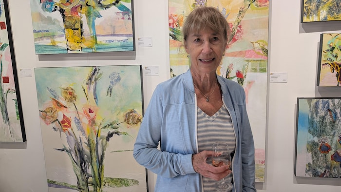 Une femme pose devant des peintures qui sont accrochées au mur.