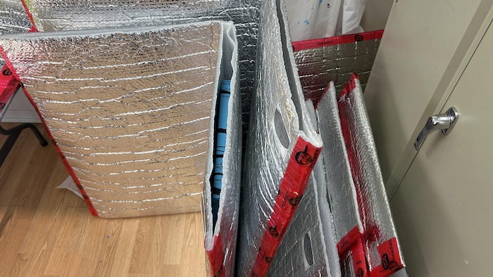 Des emballages avec fini aluminium. À l'intérieur, on aperçoit une toile peinte.