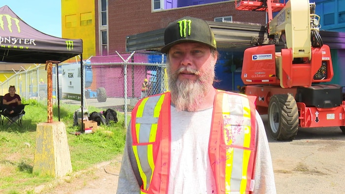 Un homme avec une grosse barbe qui porte une veste fluorescente et une casquette noire.