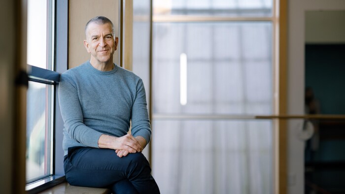 Paul Larocque, président-directeur général d'Arts Umbrella, assis sur un bord de fenêtre sourit à la caméra.