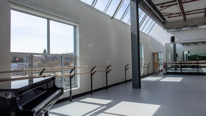 Un studio de danse éclairé par de grandes fenêtres avec un piano.