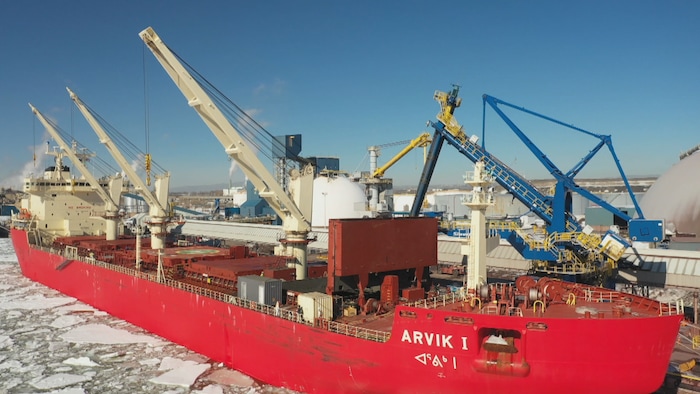 Un navire rouge est amarré à un port industriel sur des eaux glacées.