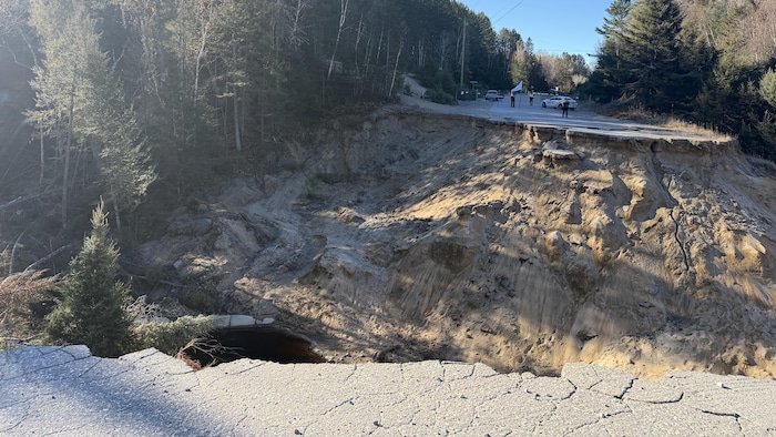 Un gouffre de plusieurs mètres sépare une route entourée d'arbres.