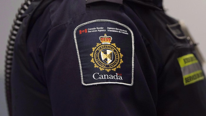 شارة وكالة الخدمات الحدودية الكندية (ASFC / CBSA) على زيّ أحد موظفيها (لا نرى وجهه).