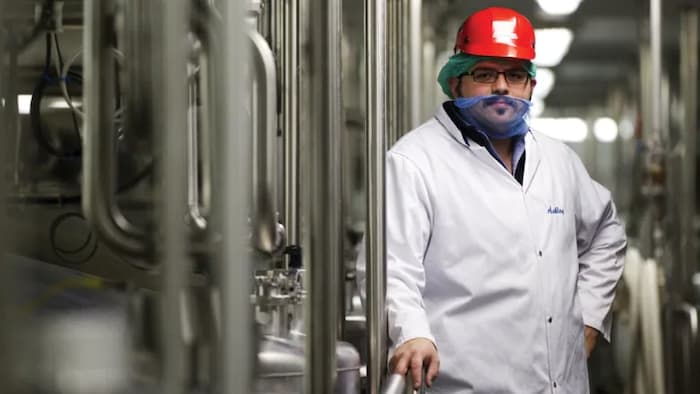 Il pose dans l'usine avec un casque sur la terre, un filet autour de la barbe.