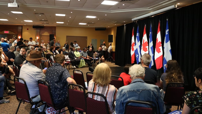 Dozens of people wait for Pierre Poilievre to appear on stage in front of them. 